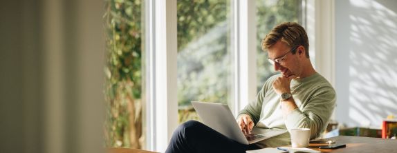Junger Mann am Esstisch arbeitet am Laptop