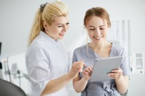 Zahnärztin und Zahnarzthelferin über ein Tablet gebeugt