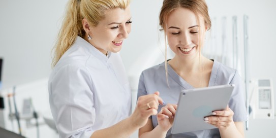 Zahnärztin und Zahnarzthelferin über ein Tablet gebeugt