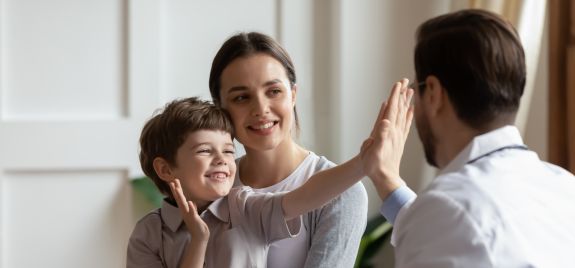 Lachender Junge mit Mutter gibt Arzt high five
