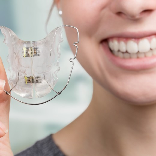 Person mit geraden Zähne hält herausnehmbare Zahnspange