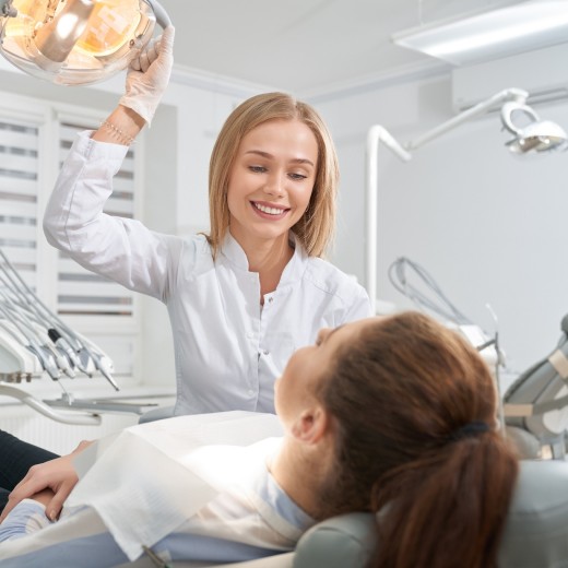 Junge Zahnärztin lächelt Patientin während einer Behandlung an